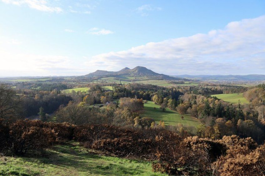 A valley with rolling hills, a mountain in the distance, and a mix of green fields and trees. 3