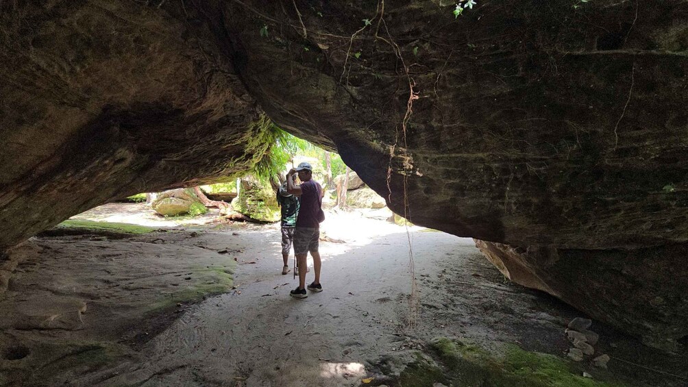 Two people standing under a large rock formation with a narrow passageway. 3