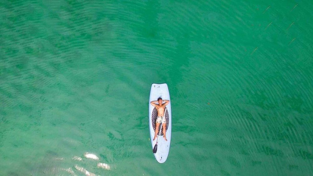 A person lying on a surfboard in clear green water. 1