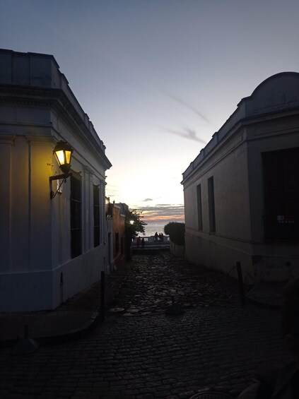 A cobblestone street flanked by white buildings with a street lamp on the left. 3