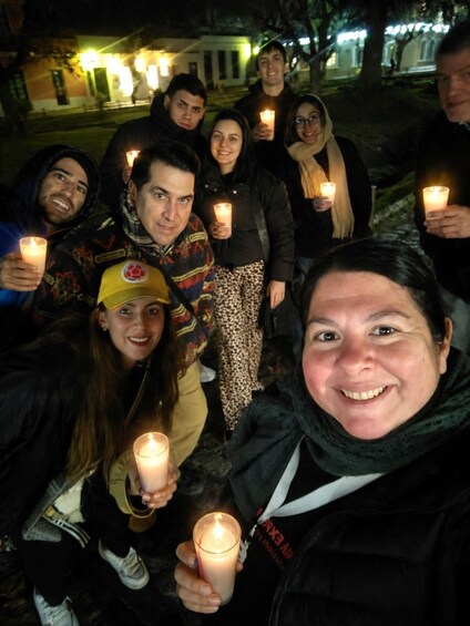 A group of people holding candles in a park at night. 1