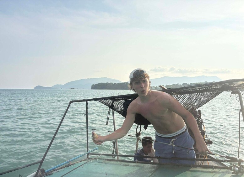 A person on a boat with a fishing net and rods, calm sea, and distant mountains. 2