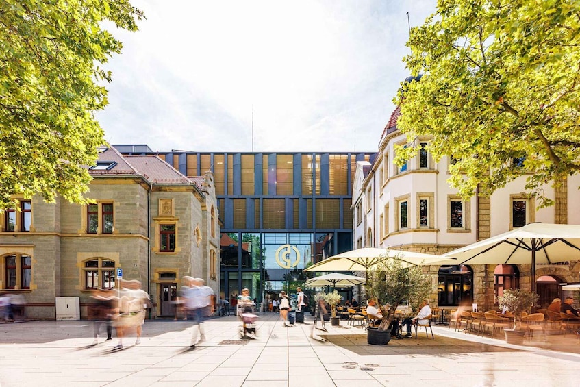 A bustling urban square with historic buildings, outdoor seating, and a modern glass entrance. 2