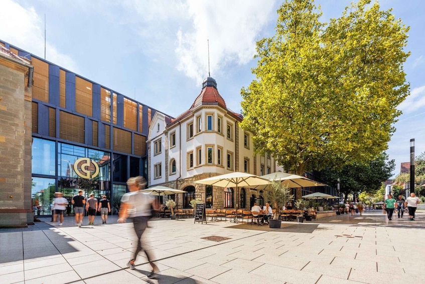 A bustling urban square with a historic building, outdoor seating, and pedestrians. 3