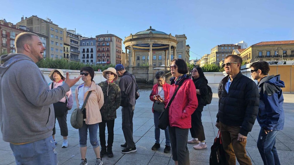 A group of people standing in a plaza with a historic building in the background. 1