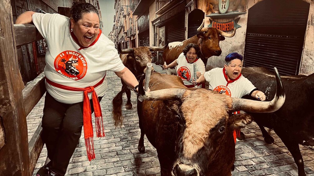 A street scene with people and bulls, some wearing white shirts with red and orange logos. 5