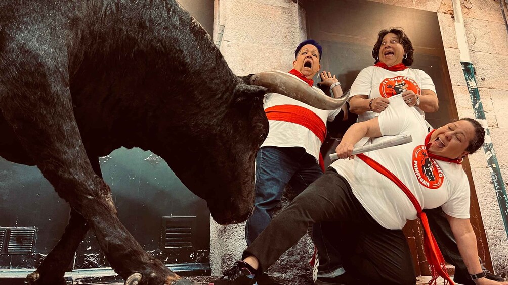 A bullfight with three people in white shirts and red sashes, one person is holding a bull's tail. 2