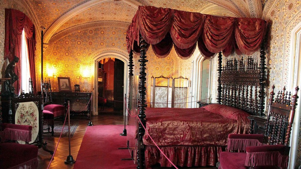 An ornate bedroom with a four-poster bed, red drapery, and intricate wall and ceiling designs. 4