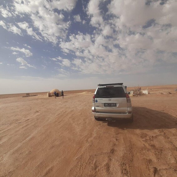 A silver SUV parked in a desert with a clear sky and scattered clouds. 3