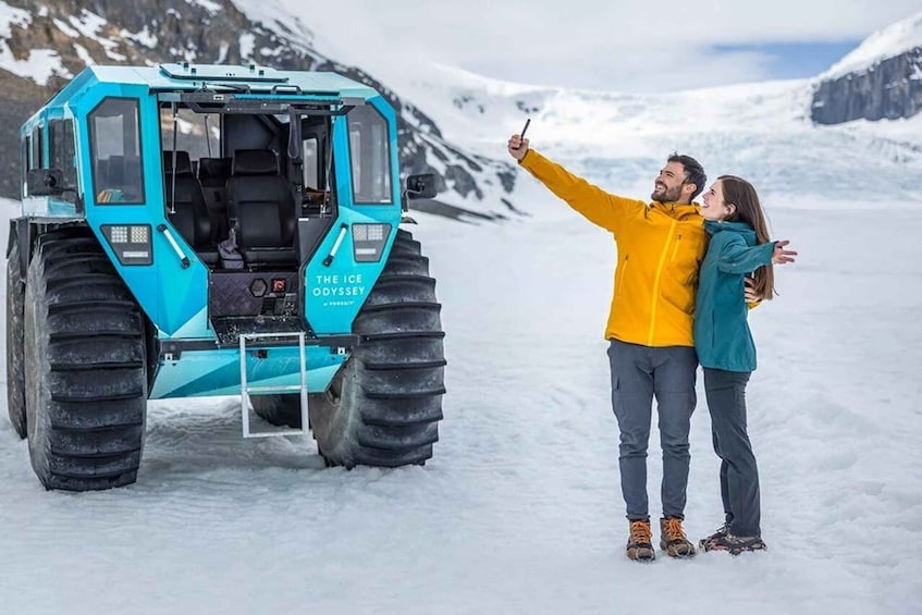 A turquoise ice rover with the text 'THE ICE ODYSSY' on its side, parked on a snowy landscape with mountains in the background. 1