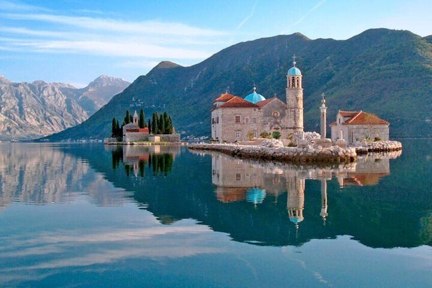 A serene lake with a historic building featuring a bell tower and domed roof, surrounded by mountains. 2