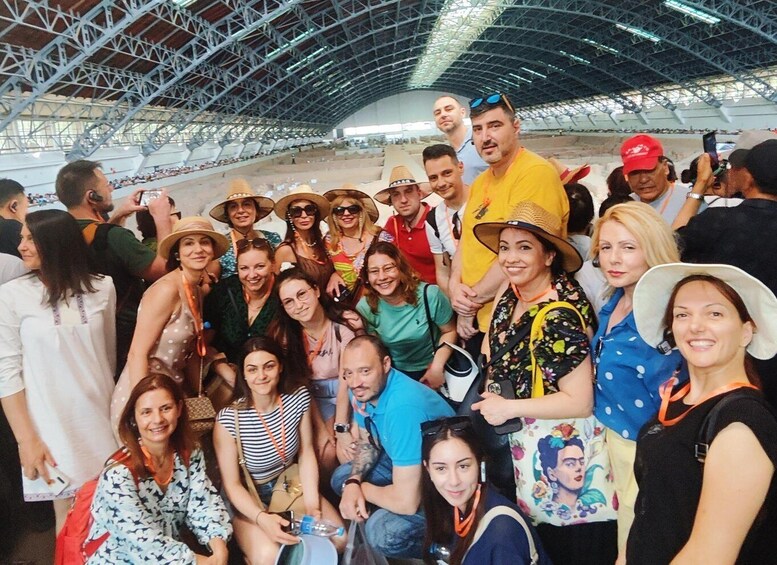 A group of people posing for a photo in an indoor venue with a high ceiling and metal framework. 1