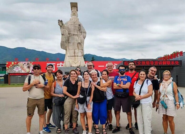 A group of people posing in front of a large statue and a building with red signage. 4