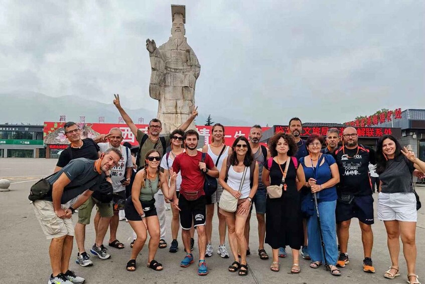 A group of people posing in front of a large statue with a mountainous backdrop. 5