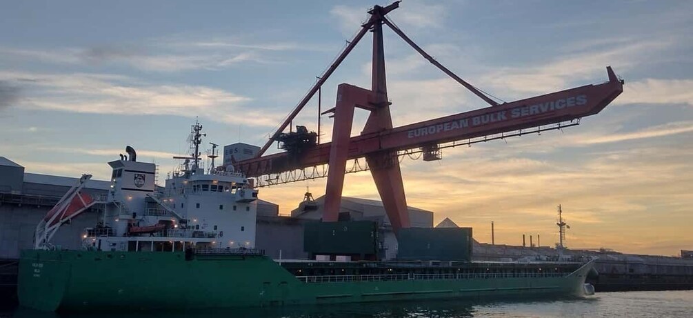 A large cargo ship with a crane labeled "EUROPEAN BULK SERVICES" at a dock during sunset. 3