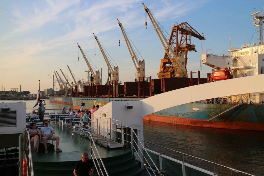 A ferry docked at a port with cranes and a large cargo ship in the background. 2