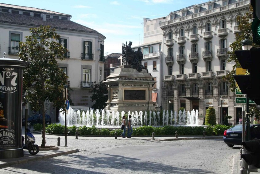 A city square with a statue, a fountain, and buildings. 5