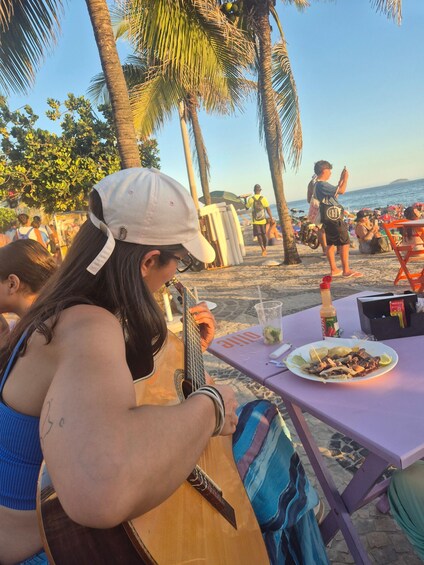A person playing a guitar at a beachside table with food and drinks. 3