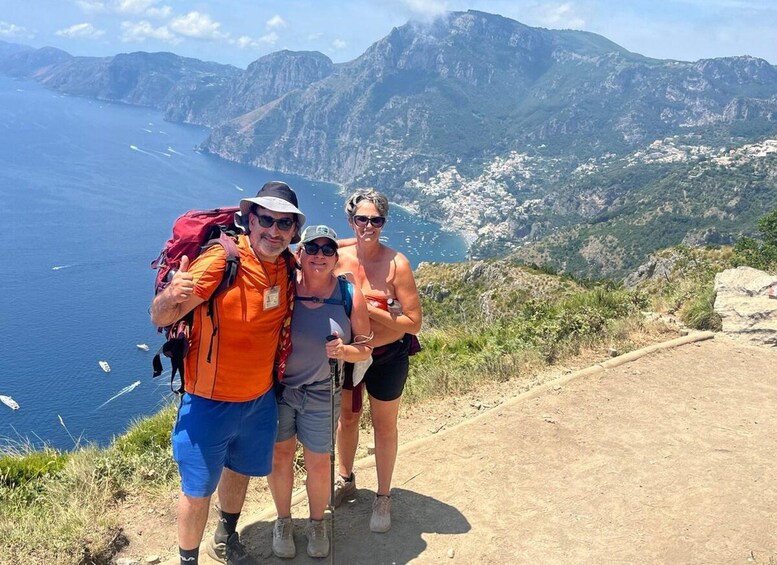 A group of hikers on a dirt path with a mountainous landscape and the sea in the background. 4