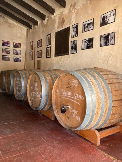 Wooden wine barrels lined up against a wall with photographs and a cross. 3
