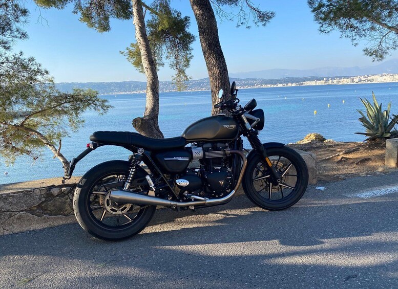 A Triumph Street Twin motorcycle parked on a coastal road with a view of the sea and a city in the background. 1