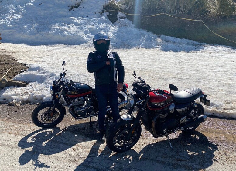 A person standing next to two motorcycles on a snowy road. 2