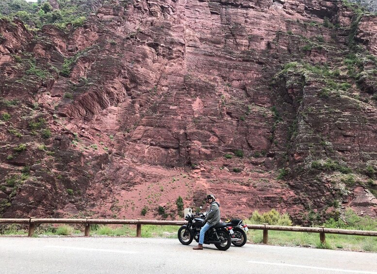 A person riding a motorcycle on a road with a rocky cliff in the background. 3