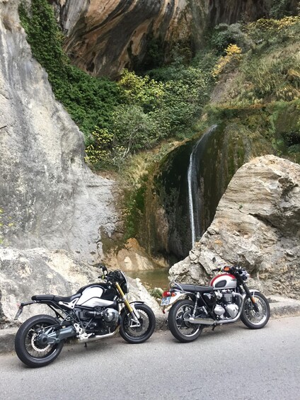 Two motorcycles parked on a road with a waterfall in the background. 4