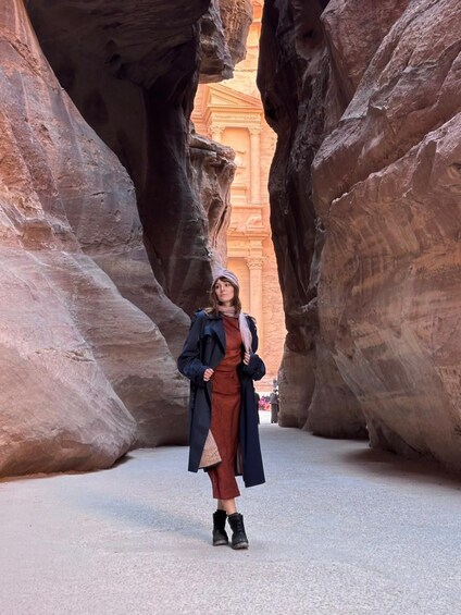 A person standing in a narrow canyon with large rock formations and a distant building. 3