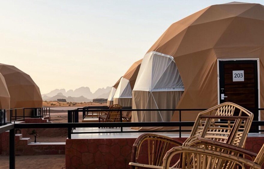 A desert landscape with tents and a balcony with wicker chairs. 5