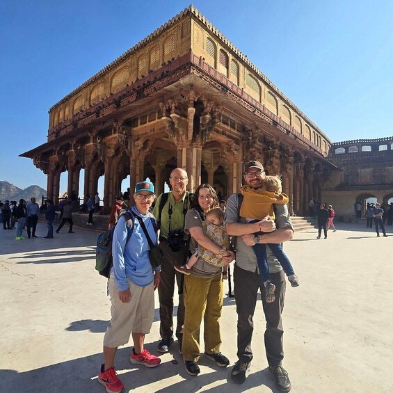 A group of people posing in front of a large, ornate building with multiple arches and columns. 2