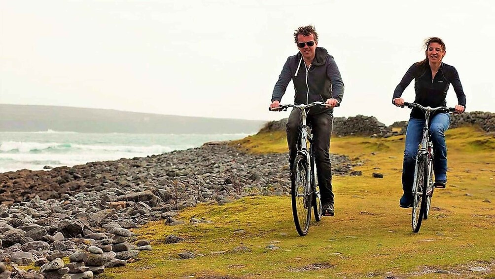 Two people riding bicycles along a rocky coastal path with the ocean in the background. 1