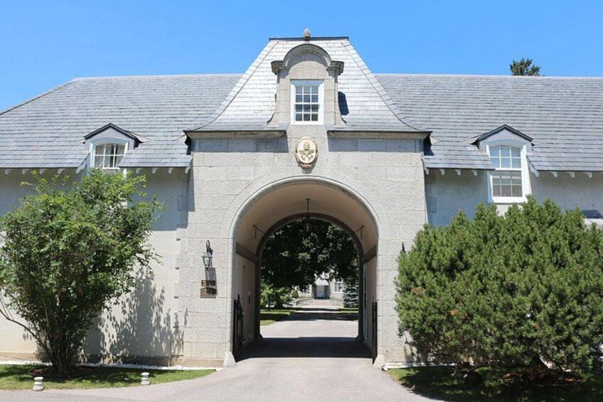 A large building with a prominent arched entrance, a clock, and a crest above the arch. 1