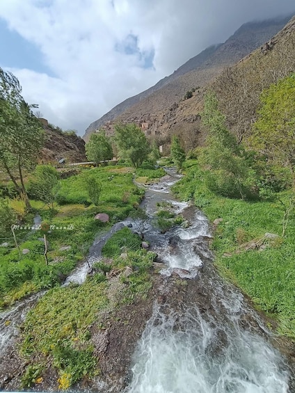A flowing river in a mountainous area with green vegetation and a village in the background. 2