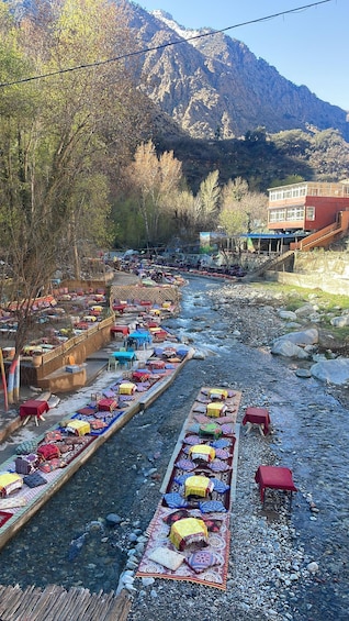 A riverside market with colorful textiles and a mountainous backdrop. 1