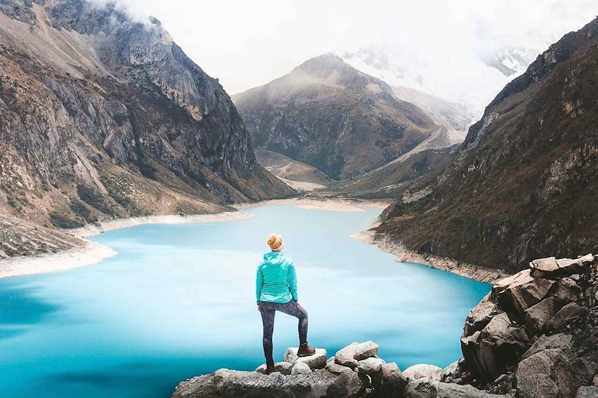 A person standing on rocks overlooking a turquoise lake surrounded by mountains. 3