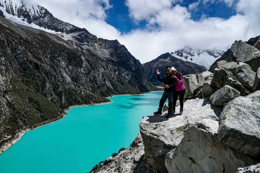 A person standing on a rocky outcrop overlooking a turquoise lake with mountains in the background. 2