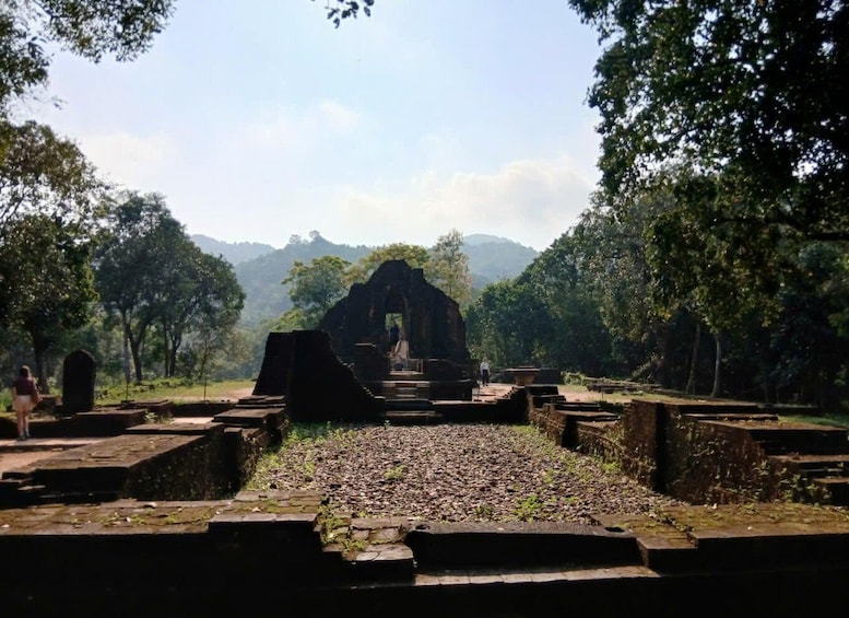 An ancient stone structure with steps leading to a central archway, surrounded by dense forest and distant mountains. 2