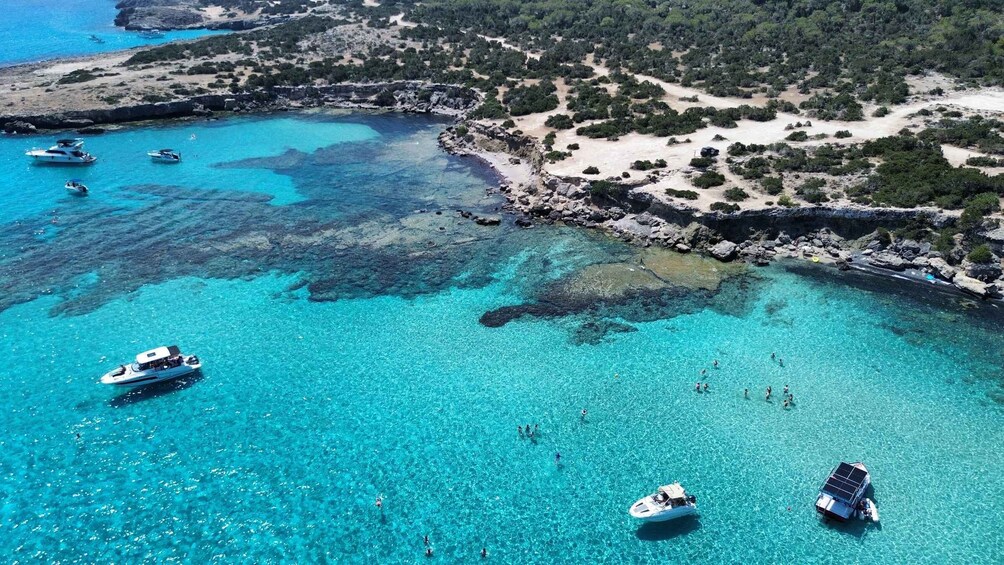 A coastal area with clear turquoise waters, boats, and people swimming. 4