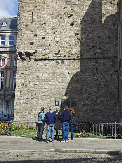 A group of people standing in front of a stone wall with plaques and a metal fence with flowers. 5