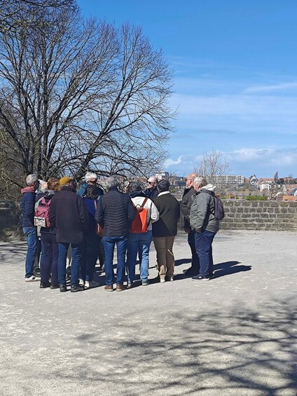 A group of people standing in a circle on a paved area with a clear sky and leafless trees in the background. 3