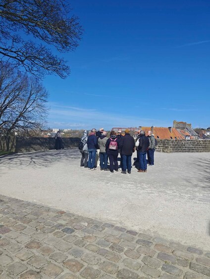 A group of people standing on a paved area with a clear blue sky and buildings in the background. 2