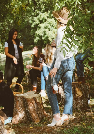A group of people sitting on tree stumps outdoors, holding drinks. 5