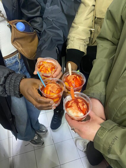 A person holding four cups of dessert with fruit and a red sauce. 4