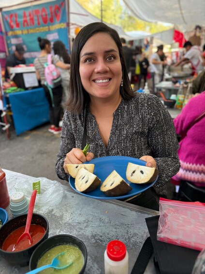 A person holding a blue plate with food items, a table with condiments, and a tent in the background. 2