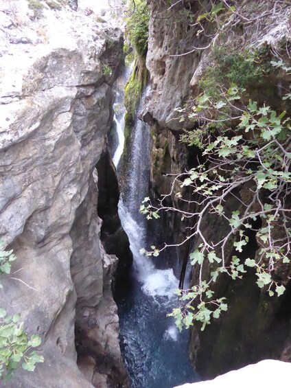 A waterfall cascading down a rocky gorge with moss-covered rocks and sparse foliage. 2