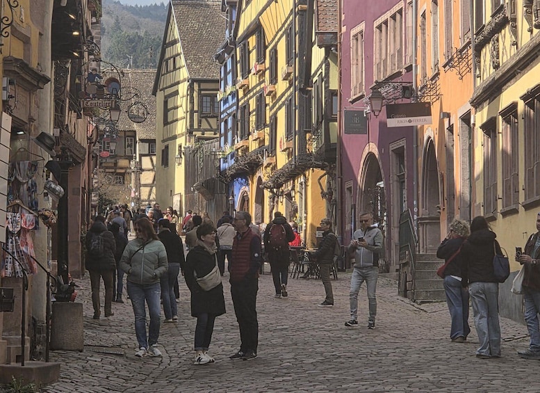 A cobblestone street lined with colorful buildings, a crowd of people, and outdoor seating areas. 2
