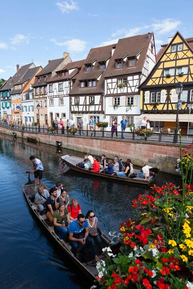 A narrow canal with boats carrying passengers, surrounded by colorful half-timbered houses and blooming flowers. 1
