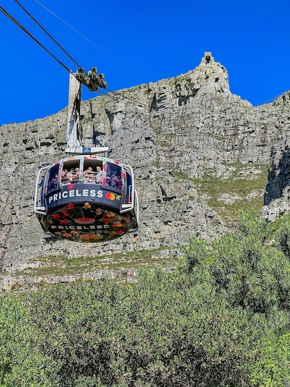 A cable car with "PRICELLES" written on it, suspended by cables against a rocky mountain backdrop. 1