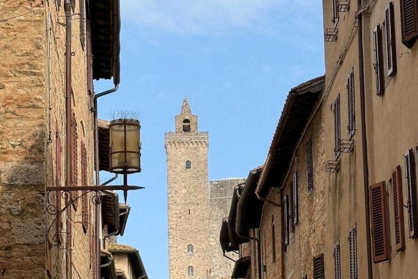 Une rue étroite bordée de vieux bâtiments, une tour de pierre et un lampadaire. 4